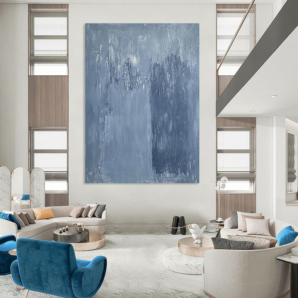 Large contemporary abstract painting in soft blue hues with textured surface and faint tree silhouettes against a deep gray background evoking calmness and emotion. DLZ1279