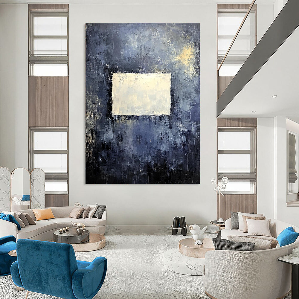 Bold contemporary abstract painting features a muted gray wall with dark blue and yellow tones highlighted by a central white square, creating a striking visual impact. DLZ0453