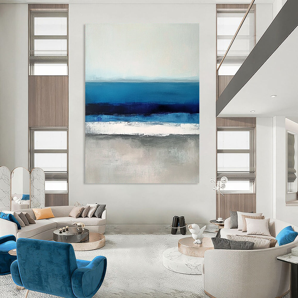 Large contemporary abstract painting featuring soft blues and grays capturing serene sea waves with a hint of deep blue for added depth. DLZ1359