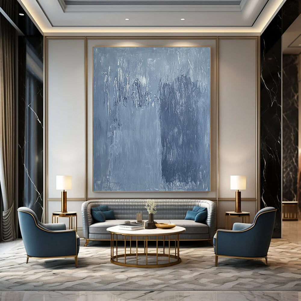 Large contemporary abstract painting in soft blue hues with textured surface and faint tree silhouettes against a deep gray background evoking calmness and emotion. DLZ1279