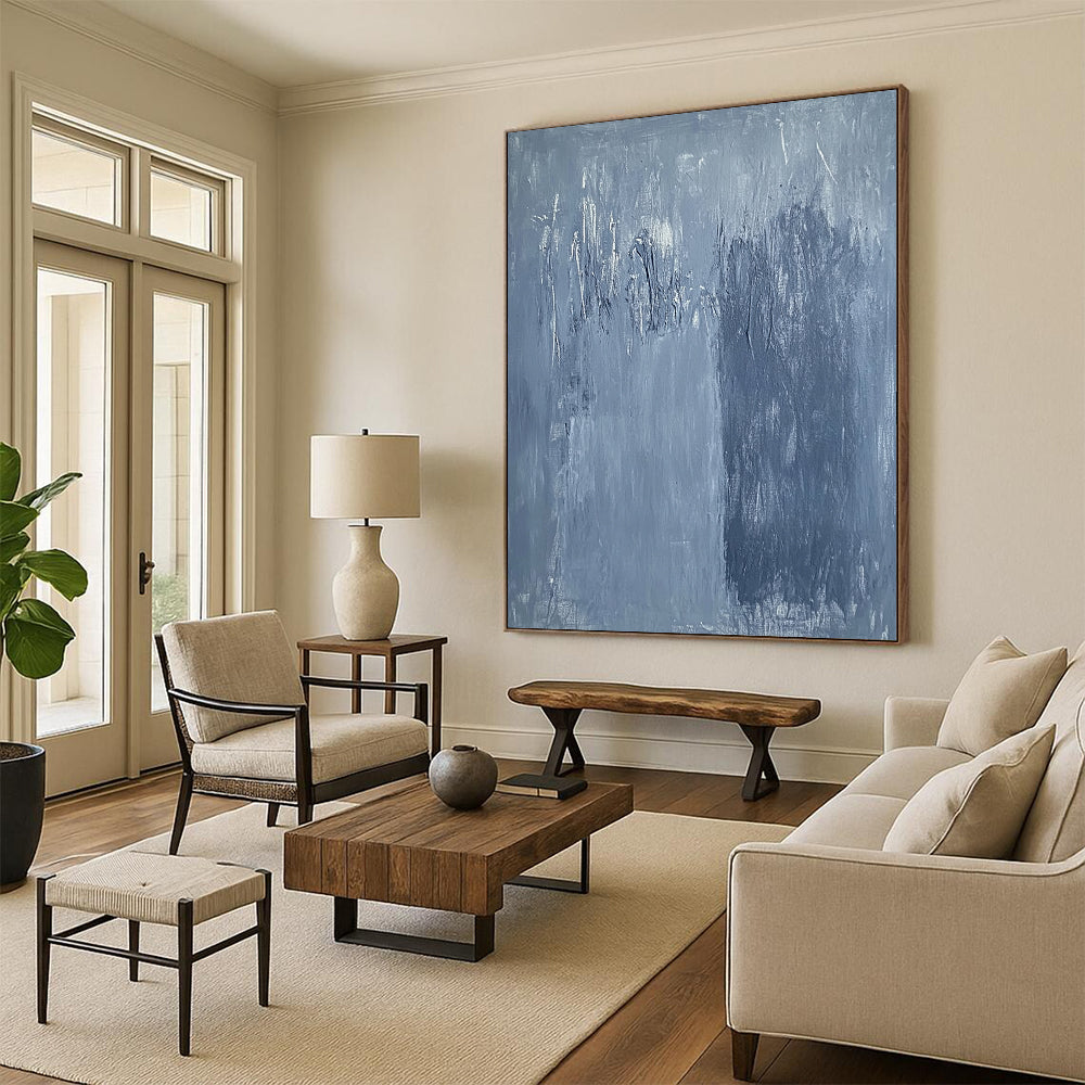 Large contemporary abstract painting in soft blue hues with textured surface and faint tree silhouettes against a deep gray background evoking calmness and emotion. DLZ1279