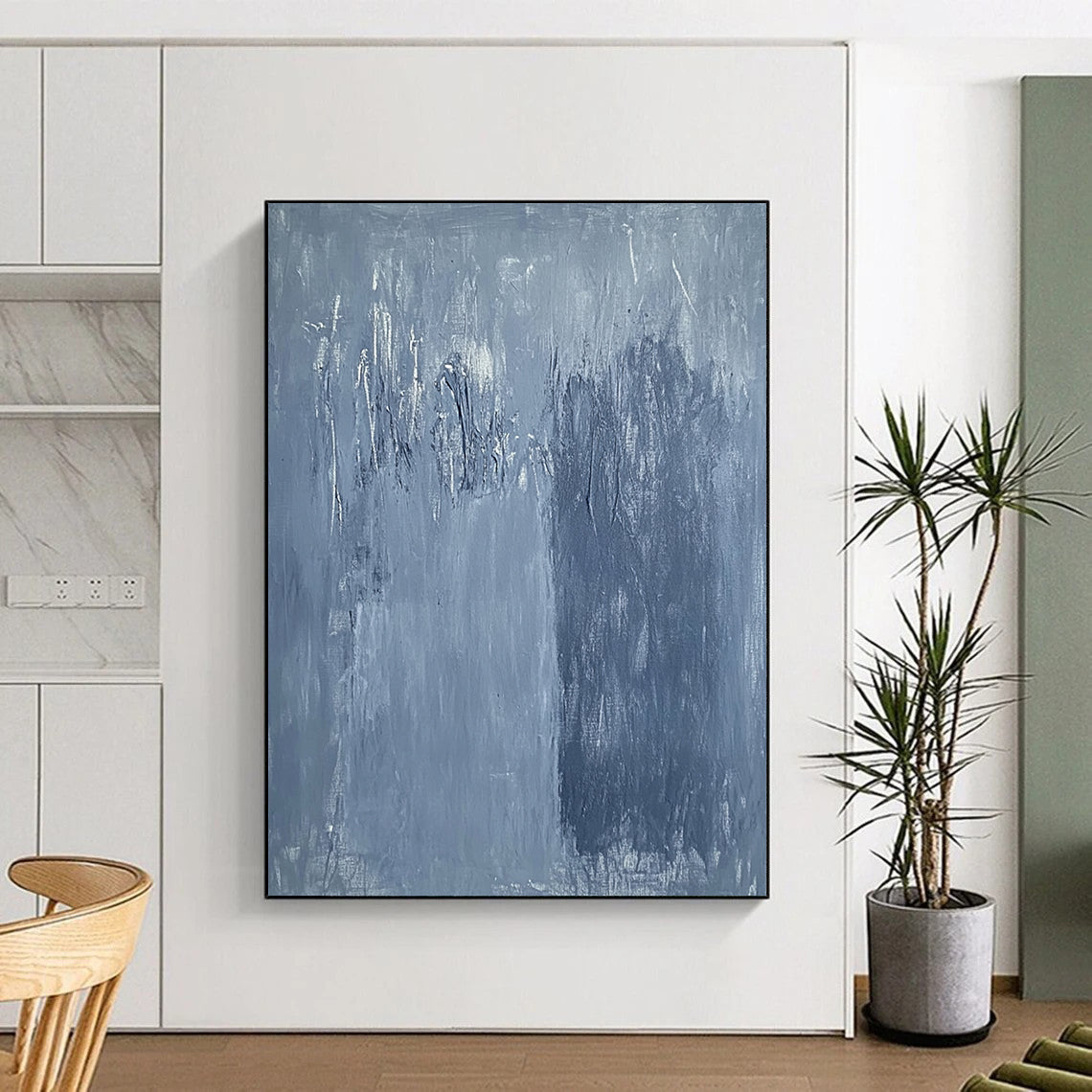 Large contemporary abstract painting in soft blue hues with textured surface and faint tree silhouettes against a deep gray background evoking calmness and emotion. DLZ1279