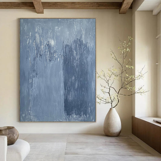 Large contemporary abstract painting in soft blue hues with textured surface and faint tree silhouettes against a deep gray background evoking calmness and emotion. DLZ1279