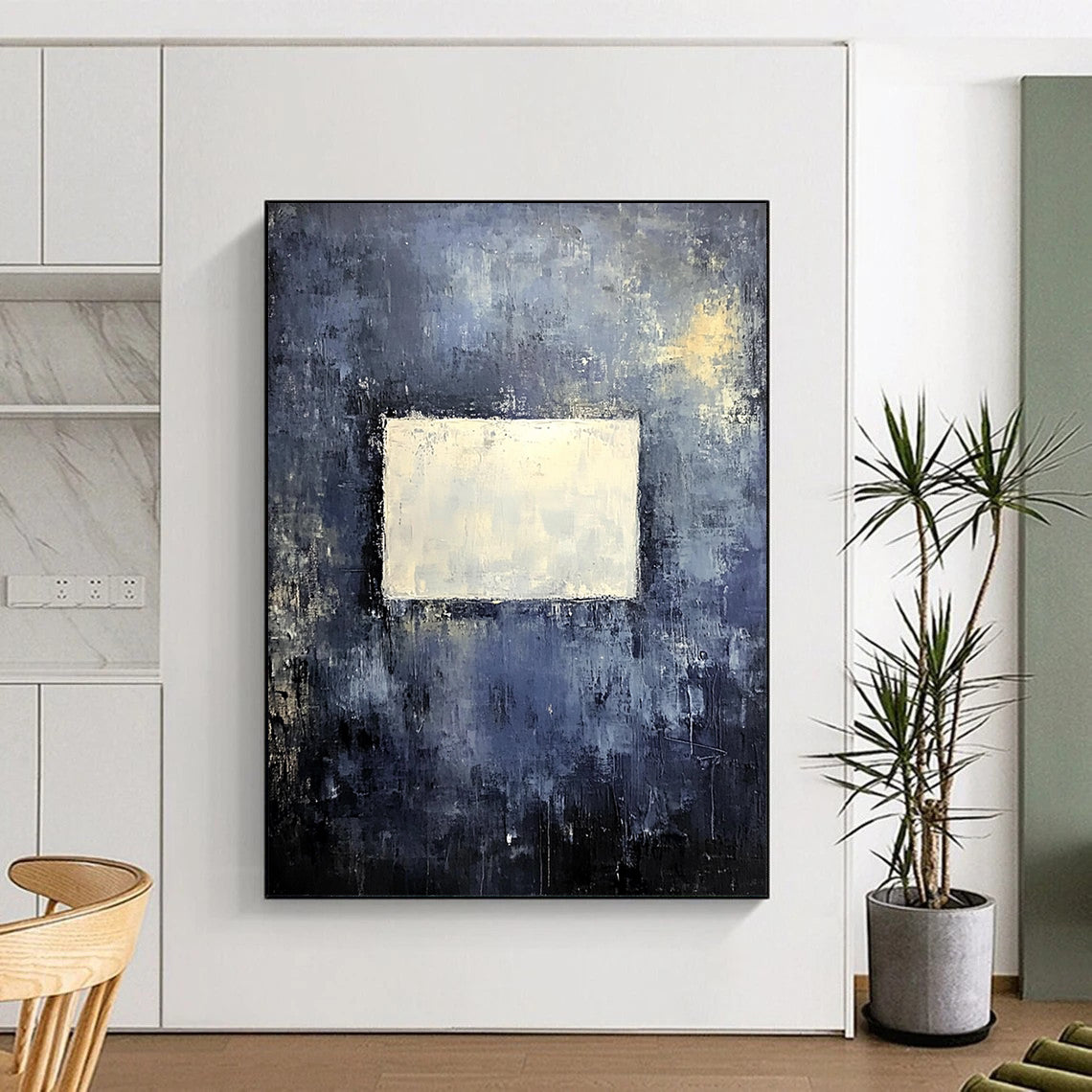 Bold contemporary abstract painting features a muted gray wall with dark blue and yellow tones highlighted by a central white square, creating a striking visual impact. DLZ0453